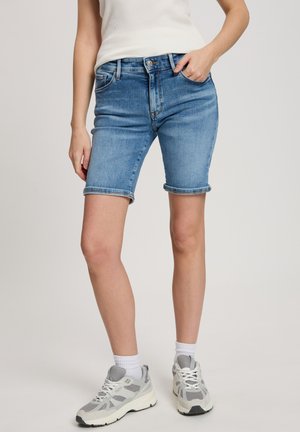 Jasnoniebieskie szorty dżinsowe w klasycznym pięciopocketowym fasonie, z podwiniętymi nogawkami i wyblakłym wykończeniem. Noszone z białymi skarpetkami do kostek i szarymi sneakersami.