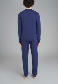 Completo da pigiama in cotone/poliestere blu navy, composto da una maglia a maniche lunghe con scollo tondo e pantaloni abbinati dotati di una vita elasticizzata e tasca laterale.