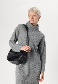 Pull en tricot gris avec un col montant et un motif en losange texturé. Associé à un sac bandoulière en cuir noir avec une seule sangle.