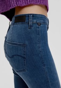 Modré džínové kalhoty s úzkým střihem, viditelným prošíváním, zadní kapsou s zakřiveným detailem a značkovou etikou na pásku.