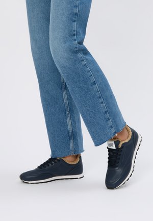 Zapatillas azul marino con un suave forro de piel, puntera redonda y suela de goma negra. Combinadas con jeans de mezclilla azul ajustados.