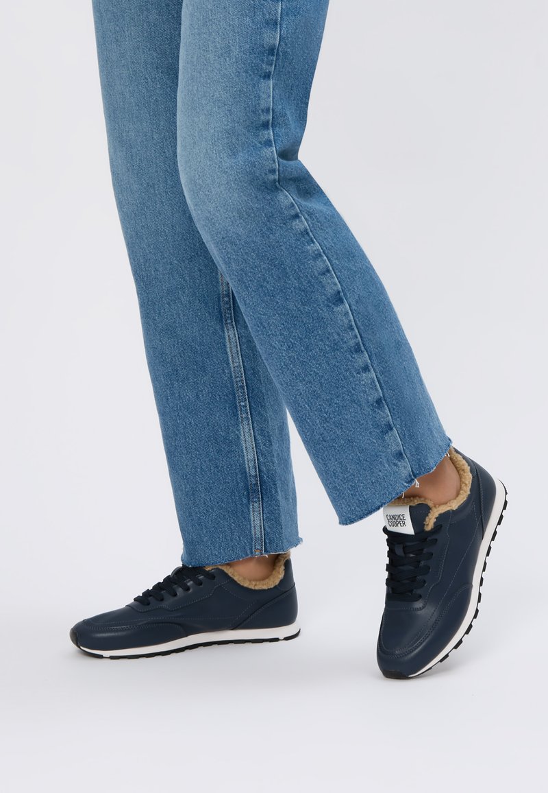 Námořnické modré tenisky s měkkou kožešinovou podšívkou, kulatou špičkou a černou gumovou podrážkou. Kombinované s zkrácenými modrými džíny.