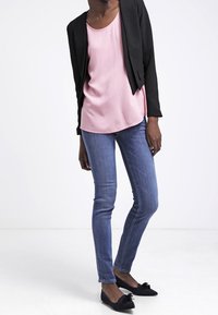 Cropped blazer nero sopra una maglietta rosa chiaro, abbinato a jeans skinny blu e ballerine nere con un accento a fiocco.