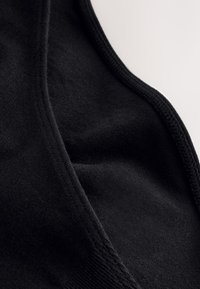 Brassière de sport noire en tissu doux au toucher lisse, présentant un design simple et une couture élastique le long des bords.