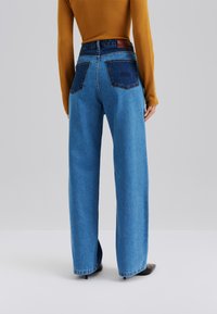 Széles szárú, magas derekú kék farmernadrág sötétkék foltzsebekkel. A szövet denim, sima tapintású és enyhén rugalmas.