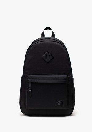Sac à dos noir en tissu durable, avec un logo en forme de diamant, une poche zippée à l'avant et des bretelles rembourrées. Design simple et fonctionnel.