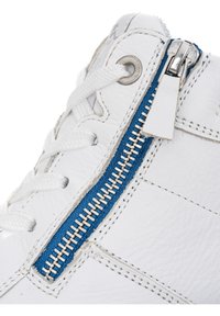 Baskets en cuir blanc avec lacets blancs et fermeture éclair métallique sur une bande de tissu bleu le long du côté.