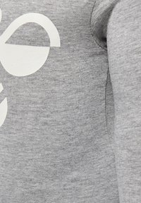 Grijze sweatshirt met een zachte textuur, voorzien van een groot wit grafisch ontwerp op de voorkant. De halslijn is rond, en de stof lijkt lichtgewicht.