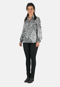 Camisa de botones en estampado animal blanco y negro, con mangas largas. Combinada con pantalones negros y botas negras de tobillo.