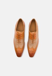 Scarpe da donna in pelle color camoscio e beige chiaro con perforazioni decorative, punta affusolata, design con lace-up e superficie liscia.