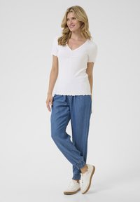 Top alb cu dungi, cu mânecă scurtă și decolteu în V, cu detalii pliate, asortat cu pantaloni jogger din denim largi, care au manșete elastice la glezne, și adidași albi.