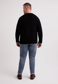 Maglione nero a maniche lunghe, collo rotondo, indossato con jeans azzurri chiari con dettagli sbiaditi e scarpe marroni con suola piatta.
