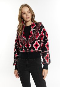 Cardigan lavorato a maglia con una base nera e vivaci motivi geometrici rossi e bianchi, colletto oversize con frange e bottoni frontali.