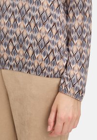 Long-sleeve top with a geometric pattern in gray, beige, and black. The fabric appears lightweight, with a slightly glossy texture.