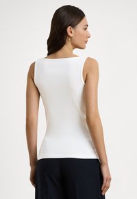 Biały, prążkowany top bez rękawów z zaokrąglonym dekoltem, gładką fakturą i dopasowanym krojem, zestawiony z ciemnymi spodniami o szerokich nogawkach.