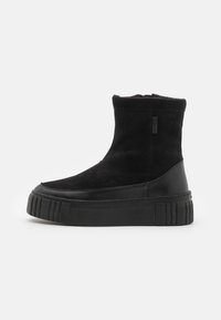 Botas ankle negras con parte superior de ante y suela de goma gruesa con ranuras verticales. Punta redondeada y diseño minimalista. Marca visible en el lateral.
