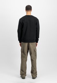 Felpa nera con polsini e orlo a coste, abbinata a pantaloni cargo oliva con molteplici tasche e vestibilità comoda. Vista posteriore mostrata.