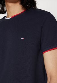 Polo blu navy in tessuto strutturato, con accenti rossi e bianchi al colletto e alle maniche, dotato di un piccolo logo ricamato.
