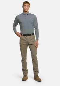 Grijze polo met lange mouwen en een kraag, gecombineerd met lichtbeige broek. Bevat een zwarte riem en tan robuuste schoenen. Casual pasvorm.