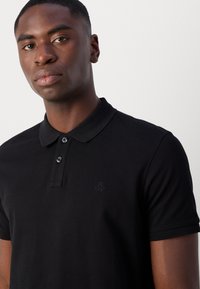 Schwarzes Poloshirt aus strukturiertem Stoff, mit drei Knöpfen, einem flachen Kragen und einem dezenten Logo auf der linken Brust.