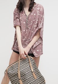 Top marrone a motivo con scollo a V e maniche larghe, abbinato a una borsa geometrica bianca e nera con dettagli color cuoio e doppi manici.