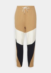 Color-blocked sweatpants in beige, cream, and black. Features a drawstring waistband and tapered cuffs. Made from soft, breathable fabric.