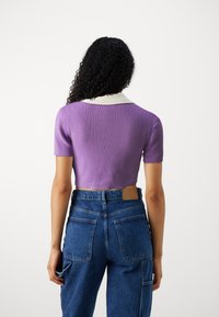 Pull court �à manches courtes en maille lavande avec un col blanc ; porté avec un jean en denim bleu taille haute doté de grandes poches arrière.