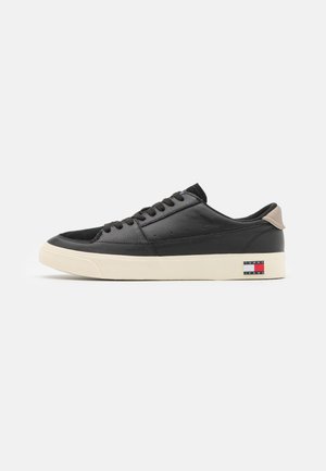 Zapatillas deportivas de cuero negro con un acabado texturizado, suela de goma color crema y tirador en el talón color marrón. Presentan acentos de logo en el lateral.