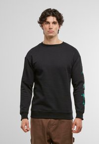 Felpa nera con scollo rotondo e maniche lunghe, con ricamo di una palma verde sul braccio sinistro. Materiale in cotone, vestibilità comoda.
