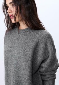 Grauer Wollpullover mit Rundhalsausschnitt, gerippten Bündchen und lockerer Passform. Weiche Textur mit subtilen melierten Details.