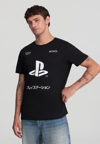 T-shirt in cotone nero con un grande logo bianco di PlayStation e testo in giapponese, design attillato, collo rotondo e maniche corte.
