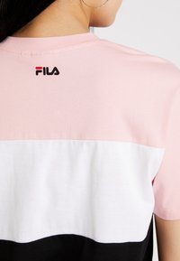 Camiseta de algodón en bloque de color rosa, blanca y negra, con mangas cortas, que presenta un pequeño logo de FILA en rojo y negro en la parte posterior del cuello.