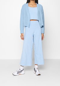 Cardigan azzurro chiaro lavorato a maglia e top corto abbinato con pantaloni a gamba larga. Tessuto morbidо, vestibilità comoda, abbinato a scarpe sportive bianche e blu navy.