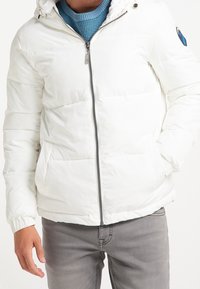 Weißer Daunenjacke mit Reißverschluss vorne, Kapuze und elastischen Bündchen. Hat eine glatte Textur und bemerkenswerte Logodetails am Arm.