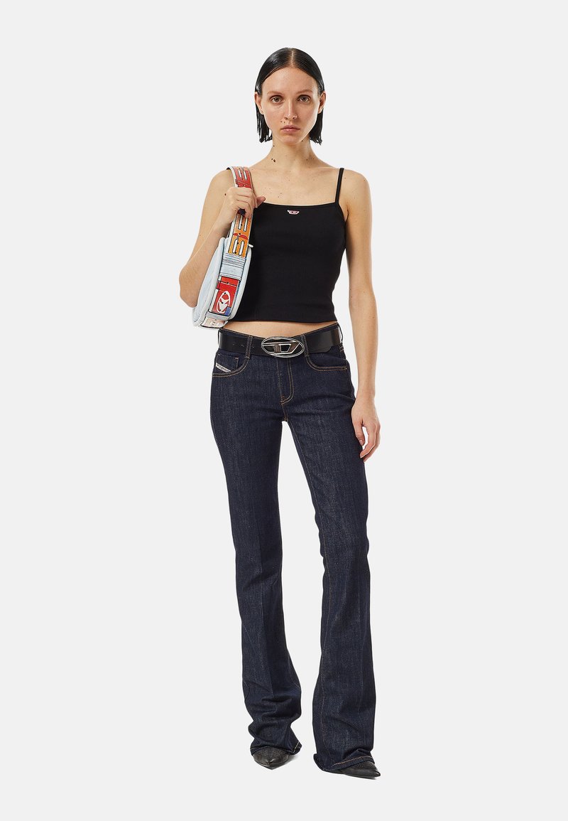 Mujer con top corto negro, jeans oscuros acampanados, cinturón negro y llevando una bolsa azul claro con una correa colorida sobre el hombro.