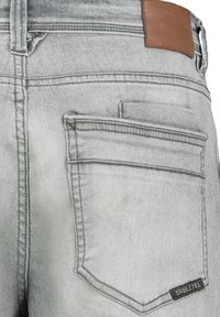 Light gray denim jeans with a leather patch at the waist, prominent stitching, and a small pocket detail on the back. Brand label visible.