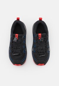 Svarta sportskor med blå accenter, nätövre, elastiskt snörningssystem och röd hälpulltab. Mönstrad sula för grepp.