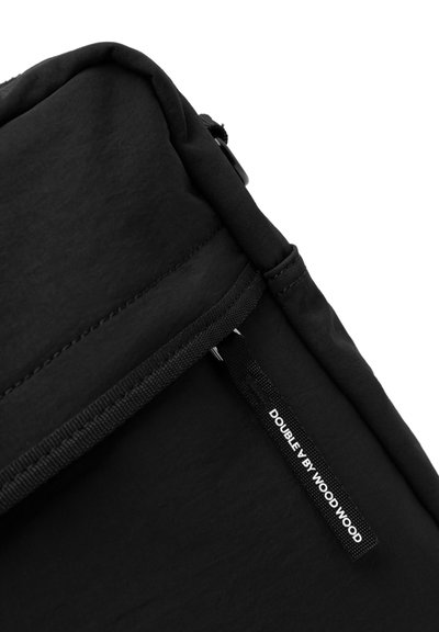 Sac à dos en tissu noir avec une texture lisse, doté d'une fermeture zippée et d'une étiquette tissée qui indique "DOUBLE BY WOOD WOOD."