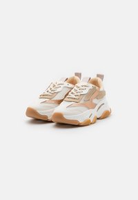 Weiße und beige Sneakers mit Mesh-Einsätzen, strukturierten Akzenten und einer dicken Gummisohle. Mit runden Schnürsenkeln und Ziehlaschen an der Ferse.