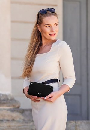 Black clutch bag with metallic accents, rectangular shape, and smooth texture. Worn with a light beige dress and black belt.