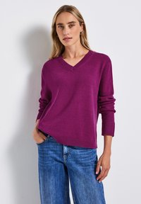 Pull en tricot violet à col en V avec des poignets et un ourlet côtelés, associé à un jean en denim bleu. La texture semble douce et légère.