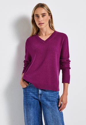 V-neck purple knit sweater with ribbed cuffs and hem, paired with blue denim jeans. Texture appears soft and lightweight.