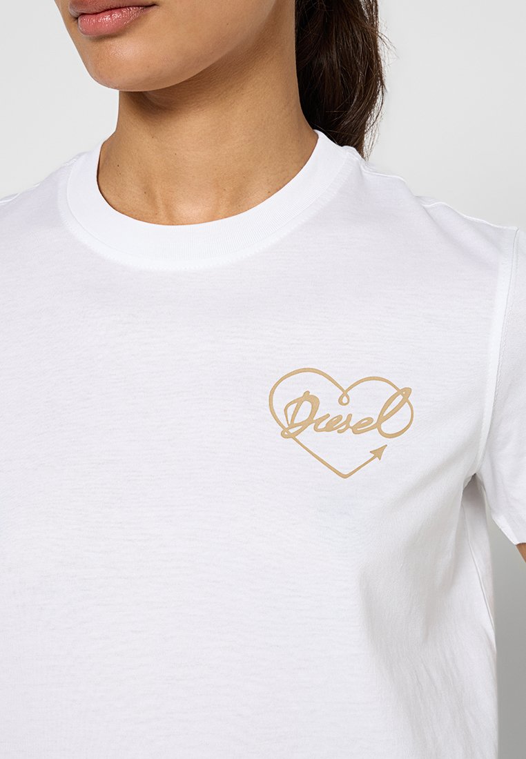 Biała bawełniana koszulka z grafiką złotego serca oraz napisem "Diesel" i akcentem strzałki na lewej stronie klatki piersiowej. Gładka faktura.