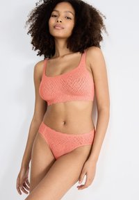 Korallfärgad lingerie-set med en strukturerad mönster; består av en crop top med breda band och vågiga kanter, tillsammans med matchande bikiniunderkläder.
