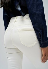 Pantalones vaqueros blancos de talle alto con bolsillos traseros, que presentan costuras planas y una textura suave. Combinados con una camisa de mezclilla oscura de botón.