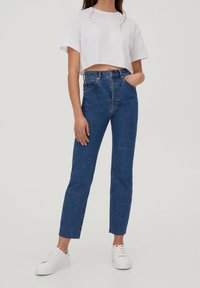 Jeans bleu taille haute en denim, à coupe droite, avec design à cinq poches et légère décoloration, assortis à un t-shirt blanc court.