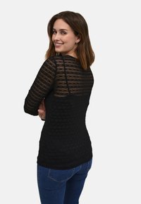 Haut noir à manches longues présentant un design texturé en côtes avec des accents transparents. Coupe ajustée avec un col rond et un ourlet arrondi.