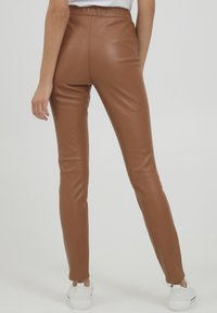 Bruine neplederen leggings met een hoge taille, gladde textuur en een aansluitende pasvorm, gecombineerd met witte sneakers.