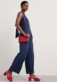 Tumesinine ülikond valgete täppidega, laiad sääred ja ilma varrukateta disain. Kombineeritud roosade platvormisandaalide ja väikese punase õlakotiga.