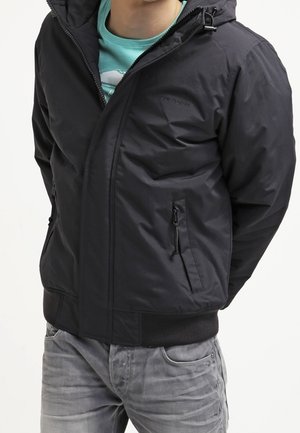 Czarna ocieplana kurtka z kapturem, z zapięciem na zamek z przodu i bocznymi kieszeniami, elastycznymi mankietami oraz gładką fakturą. Nosi kurtkę na turkusowej koszulce.